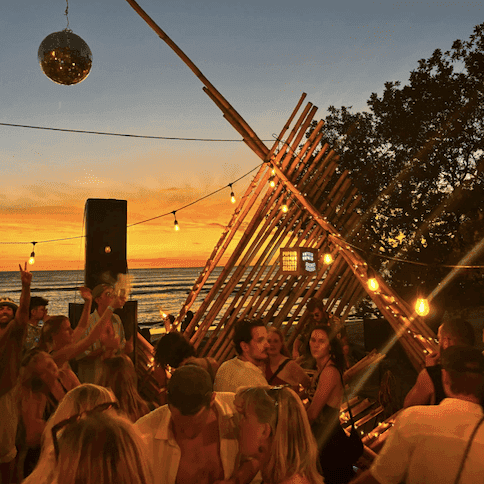 Photo of a DJ and dancers on the beach at sunset