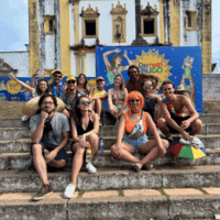 Group of travellers sitting on steps in front of a yellow and white church