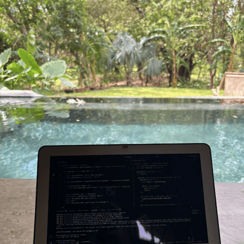 Photo of a laptop next to a pool surrounded by lush greenery